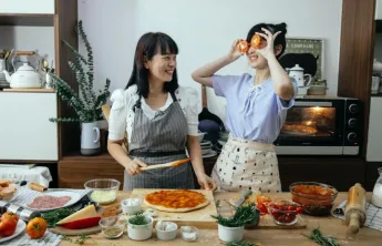 Two individuals making pizza in the kitchen 